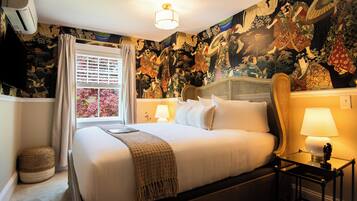 A hotel room with a large bed, two bedside lamps, a window with curtains, and a wall with a detailed tapestry.