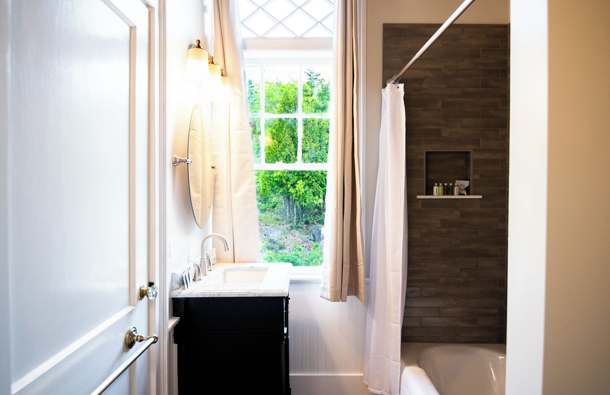 A bathroom with a white sink, a mirror, a shower area with a glass door, and a shelf with toiletries.