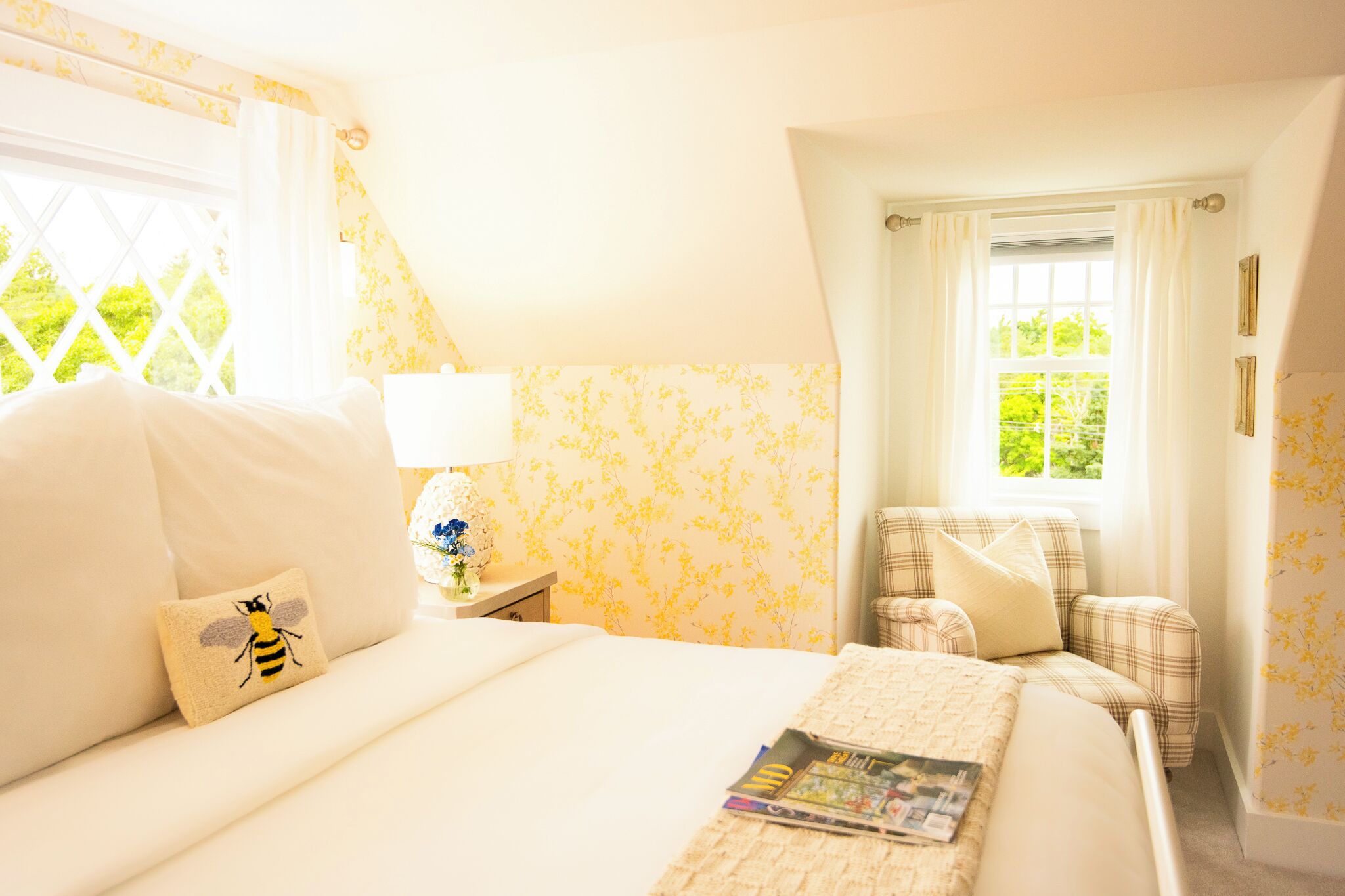 Une chambre à coucher avec un lit, une chaise, une table de chevet et une fenêtre avec des rideaux.