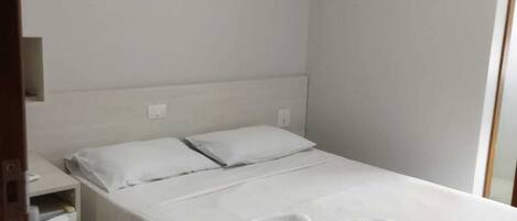 A single-bed room with a white bedspread, two pillows, a bedside table, and a towel on the bed.