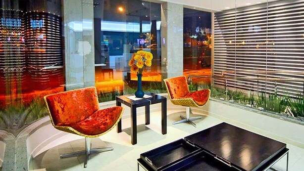Un interior moderno con dos sillas rojas, una pequeña mesa y un amplio ventanal con vistas a la ciudad.
