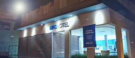 A hotel entrance with a closed shutter, a sign reading "MFG HOTEL", and a banner stating "ESTAMOS AFENDENDO".