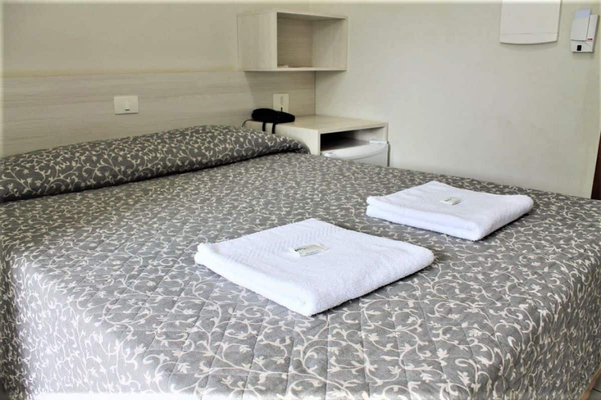 A hotel room with a bed, two pillows, a bedside table, and a wall-mounted phone.