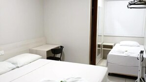 Habitación de hotel con dos camas, un escritorio pequeño, una silla, baño con espejo y un tendedero.