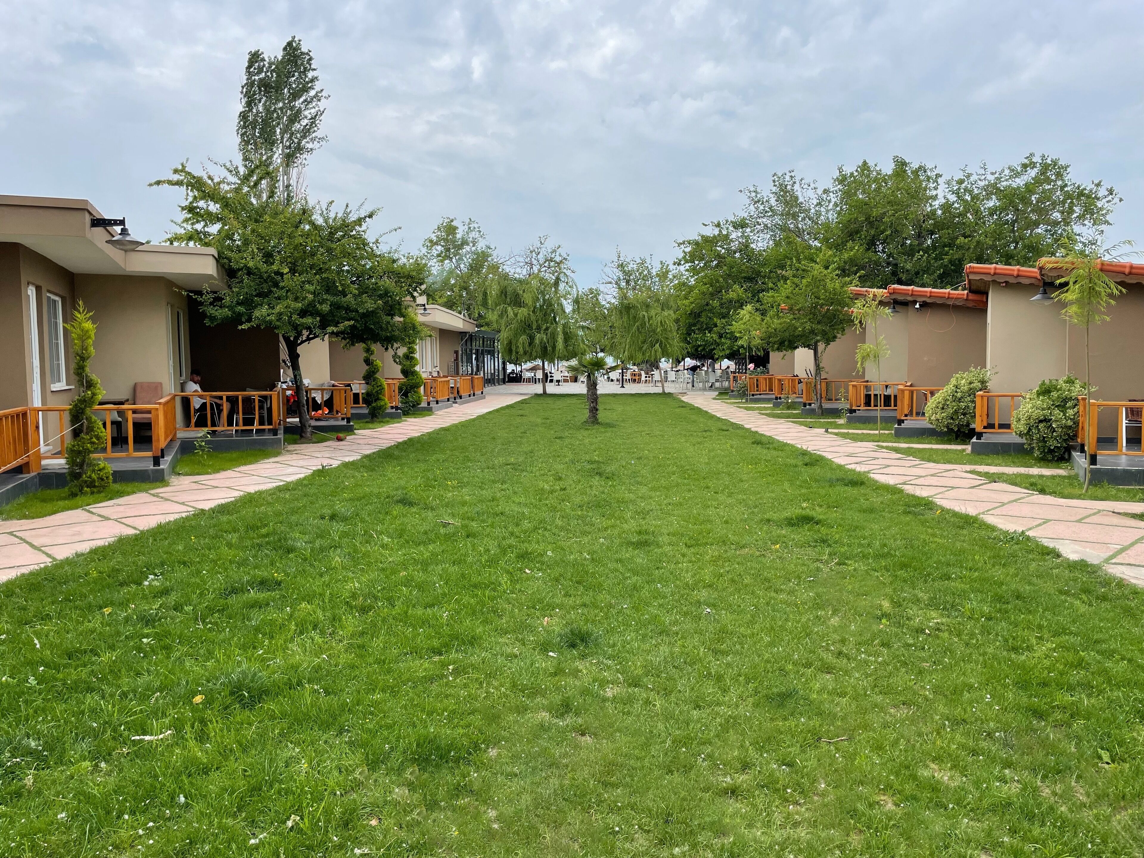 A hotel courtyard with a central lawn, outdoor seating areas, and a row of guest rooms on either side.