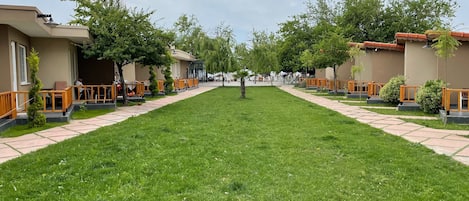 A hotel courtyard with a central lawn, outdoor seating areas, and a row of guest rooms on either side.