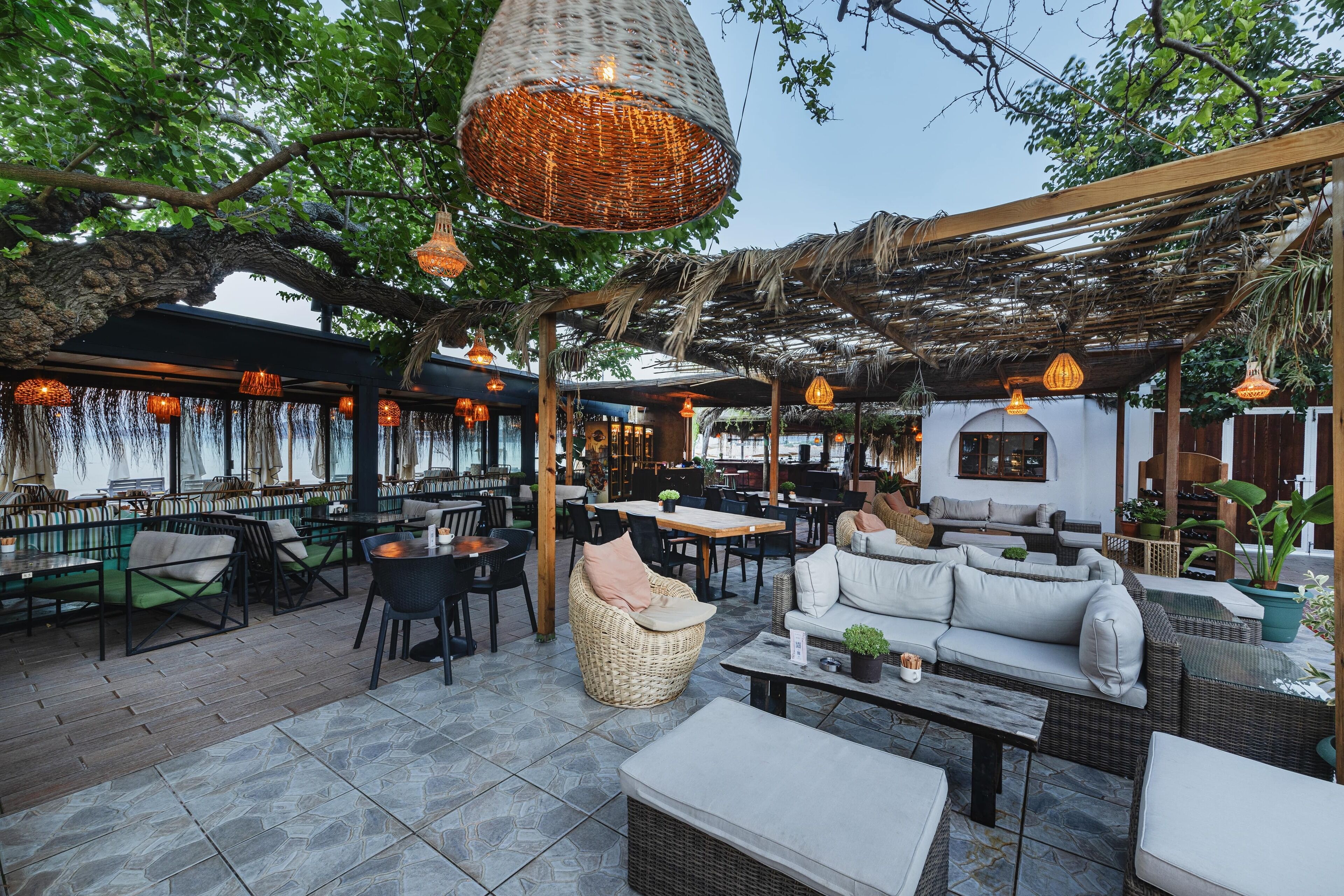 An outdoor seating area with wicker furniture, hanging lights, and a pergola structure.