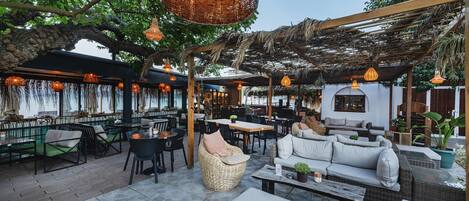 An outdoor seating area with wicker furniture, hanging lights, and a pergola structure.