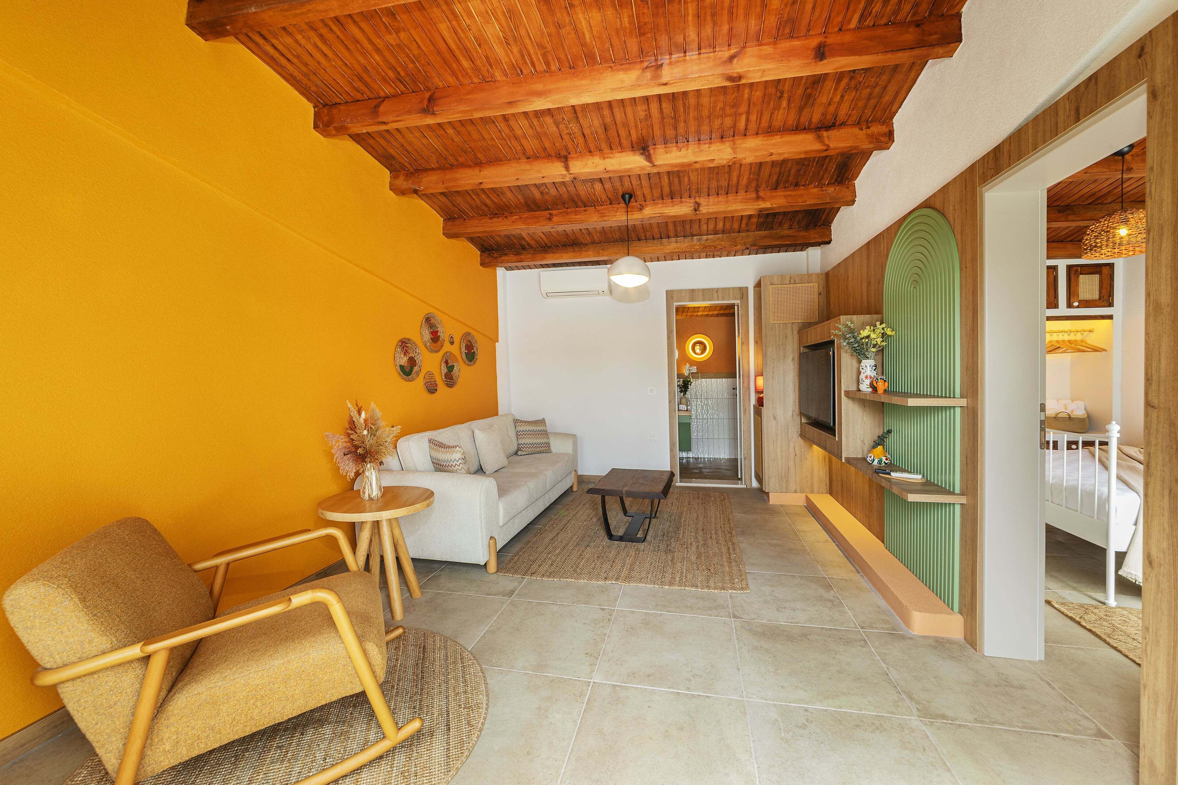 A living room with a wooden ceiling, a sofa, a chair, a small table, and a green accent wall.