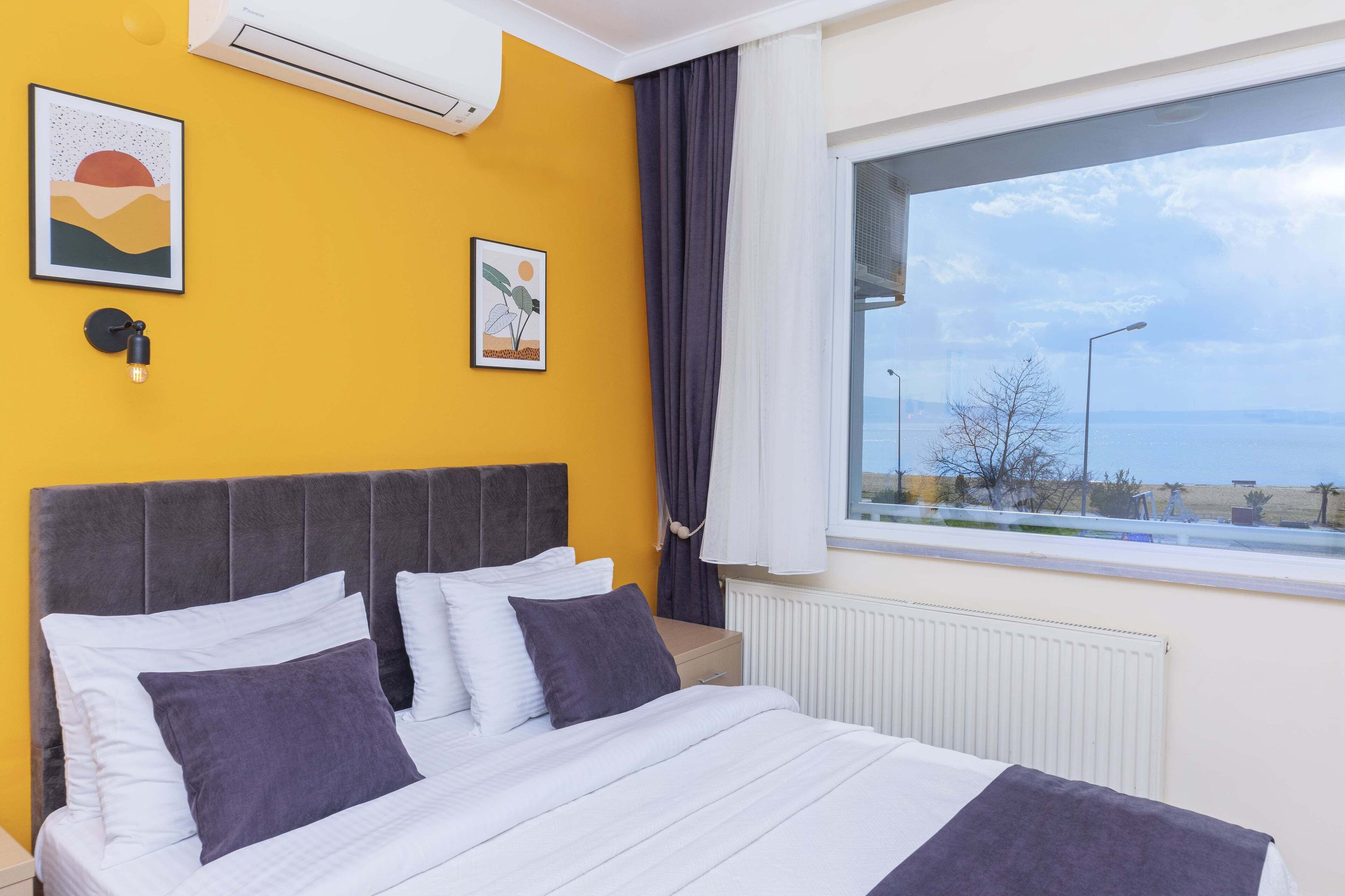 A hotel room with a bed, a window with a view of the sea, and artwork on the walls.