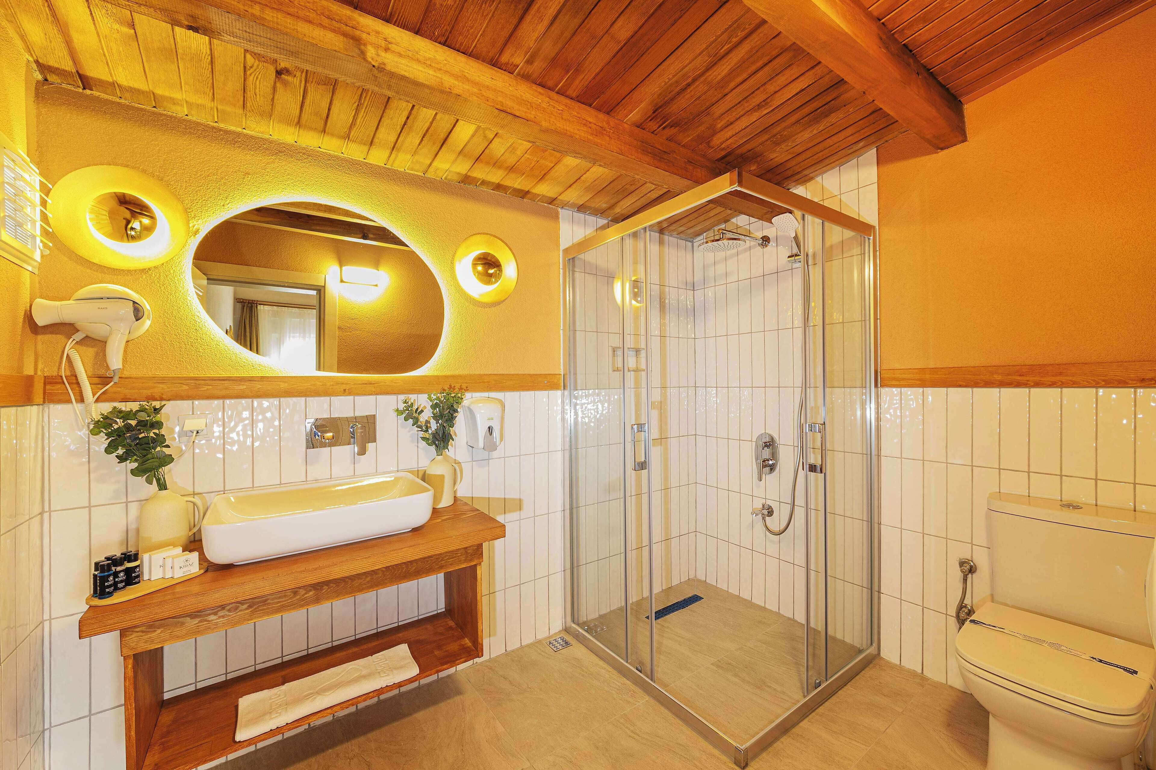 A bathroom with a wooden vanity, a large mirror, a glass-enclosed shower, and a toilet.