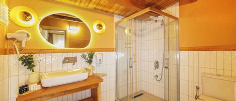 A bathroom with a wooden vanity, a large mirror, a glass-enclosed shower, and a toilet.