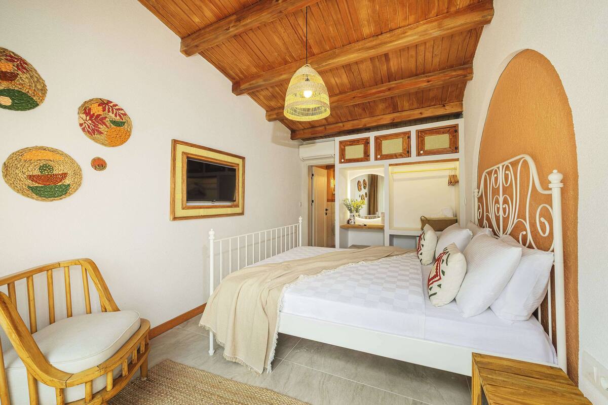 A bedroom with a wooden ceiling, a bed with white bedding, a wooden chair, and decorative woven items on the wall.
