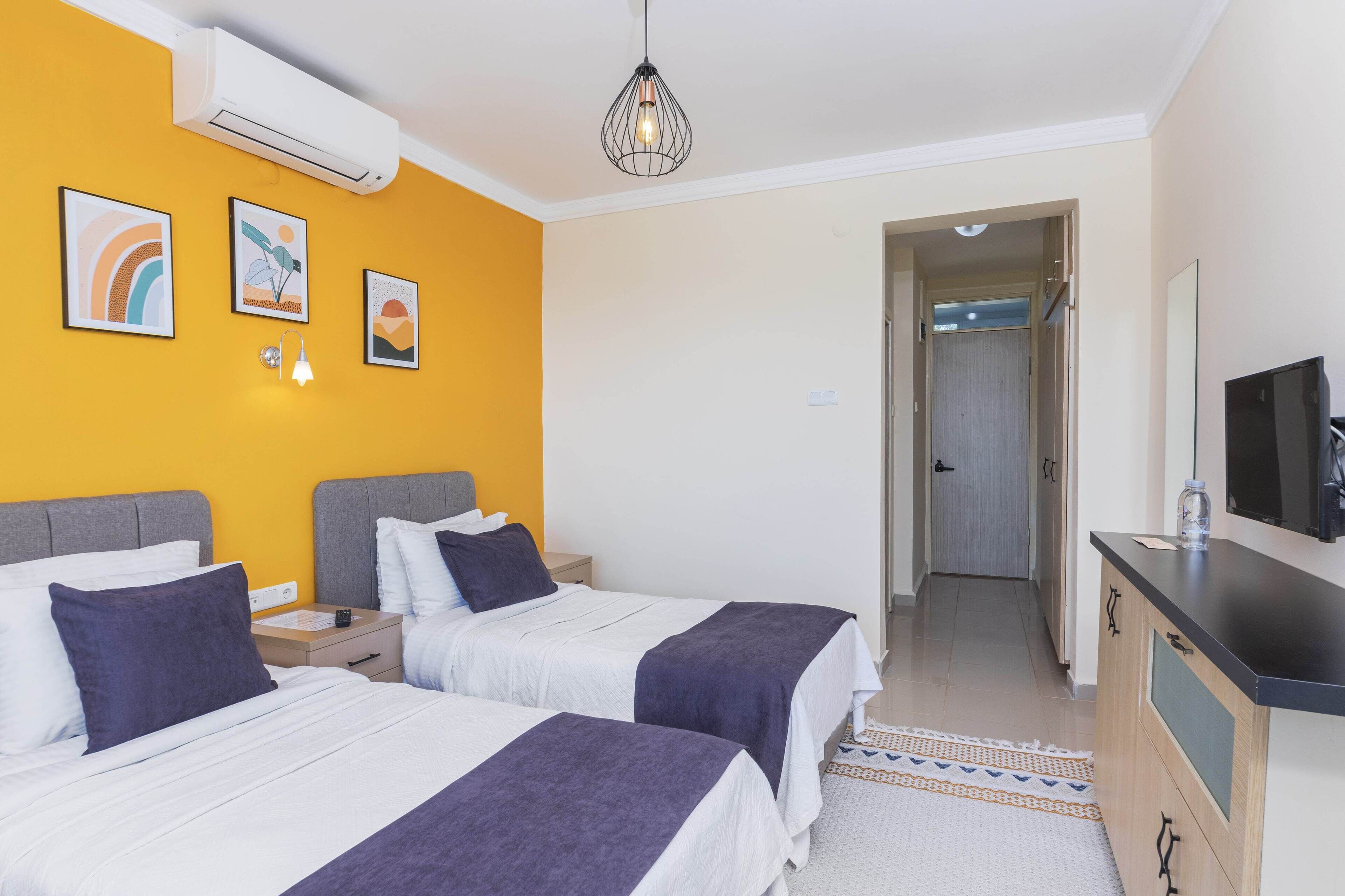 A hotel room with two beds, a TV, a desk, and artwork on the wall.