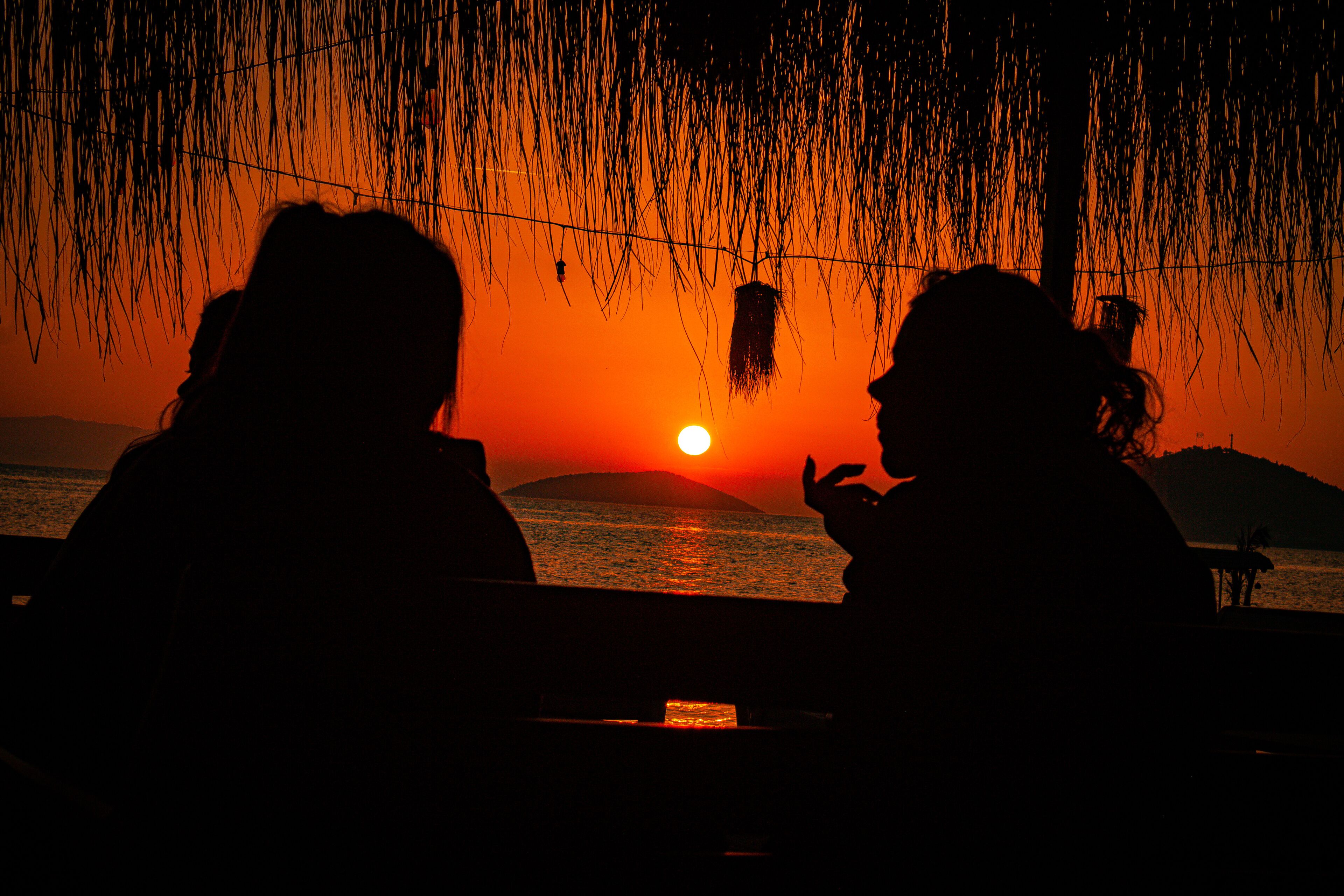 Zwei Silhouetten von Personen, die an einem Tisch sitzen, mit Sonnenuntergang im Hintergrund.