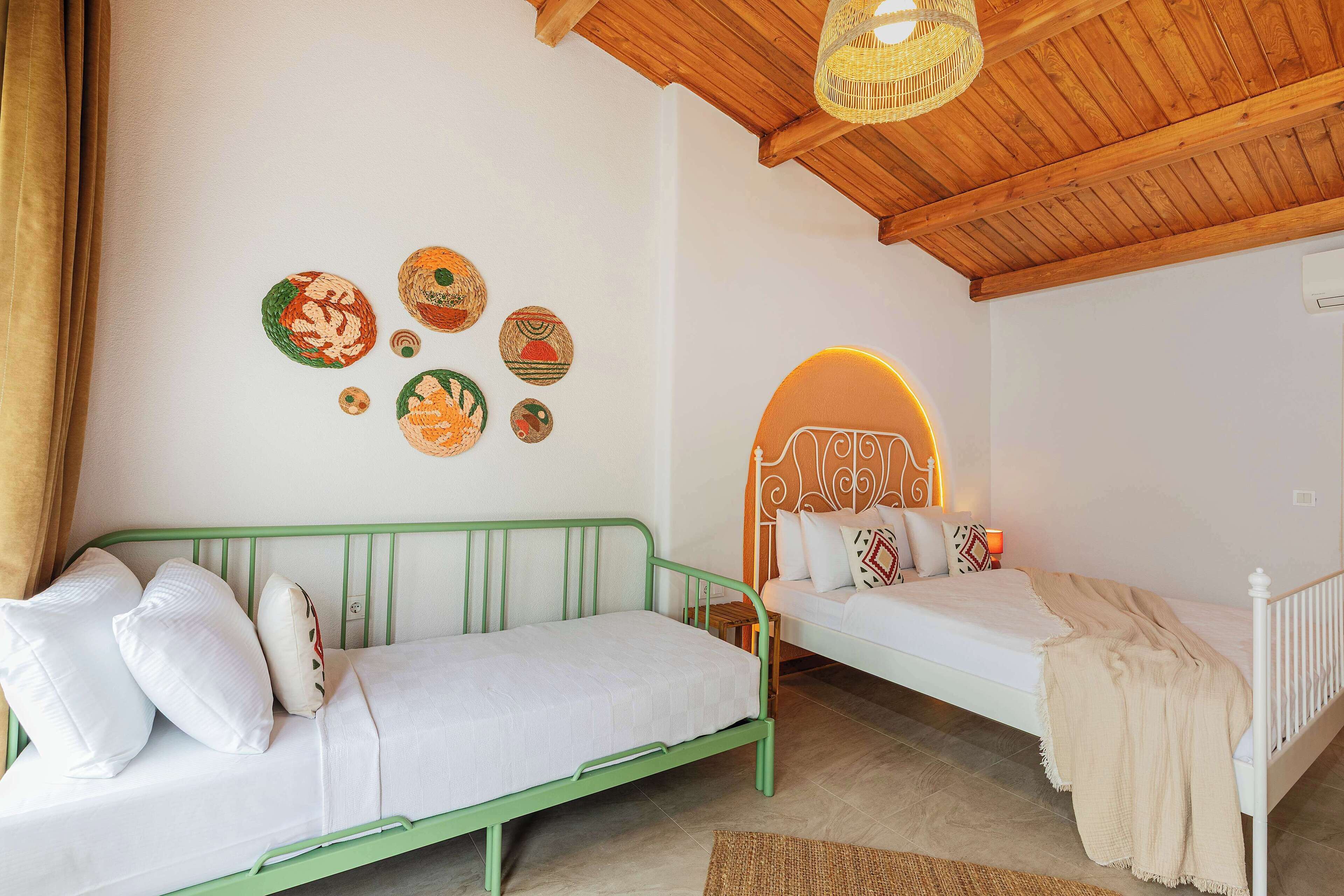 A room with two beds, one green and one white, with a woven rug on the floor.