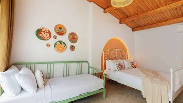 A room with two beds, one green and one white, with a woven rug on the floor.