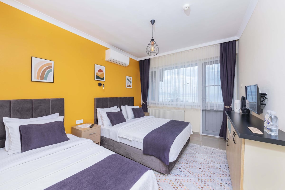 A hotel room with two beds, a desk, a chair, a window with curtains, and artwork on the walls.