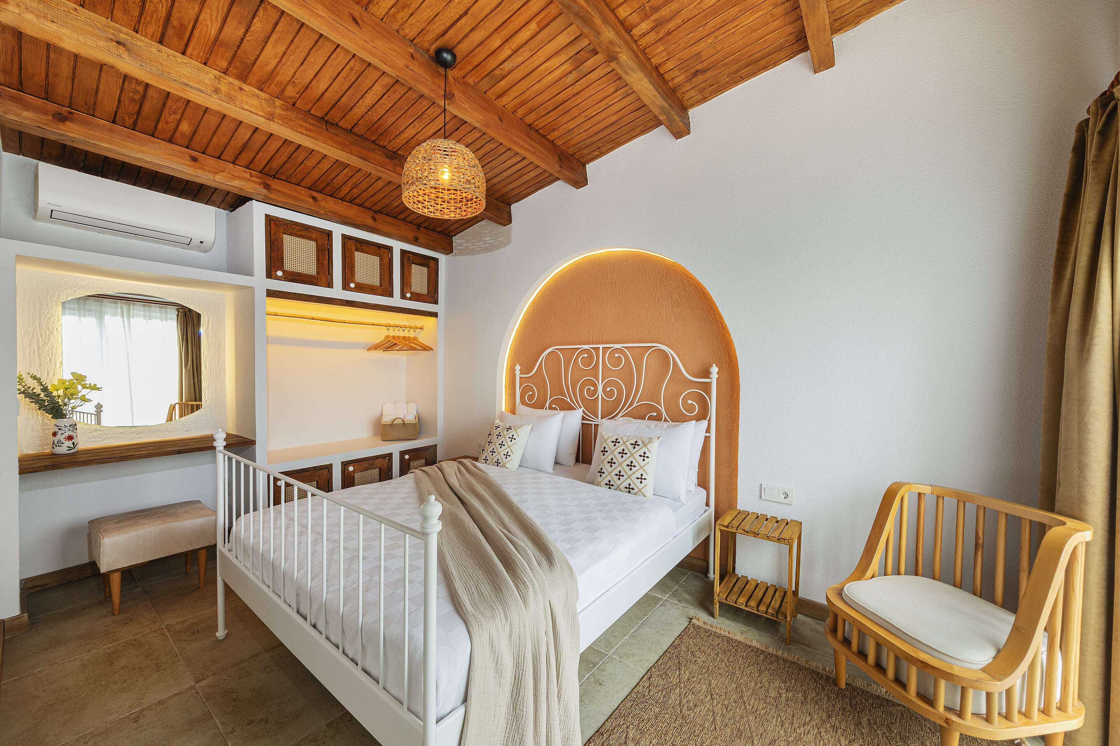 Una camera da letto con soffitto in legno, un letto con testiera bianca, un comodino, una sedia e uno specchio.