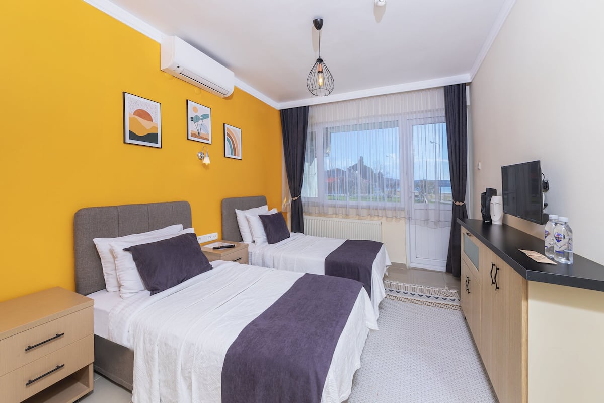 A hotel room with two beds, a desk, a chair, a window with a view, and a ceiling light.