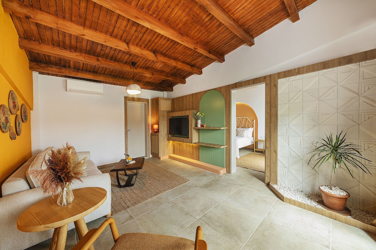 A spacious living area with a high wooden ceiling, a sofa, a coffee table, and a TV mounted on the wall.