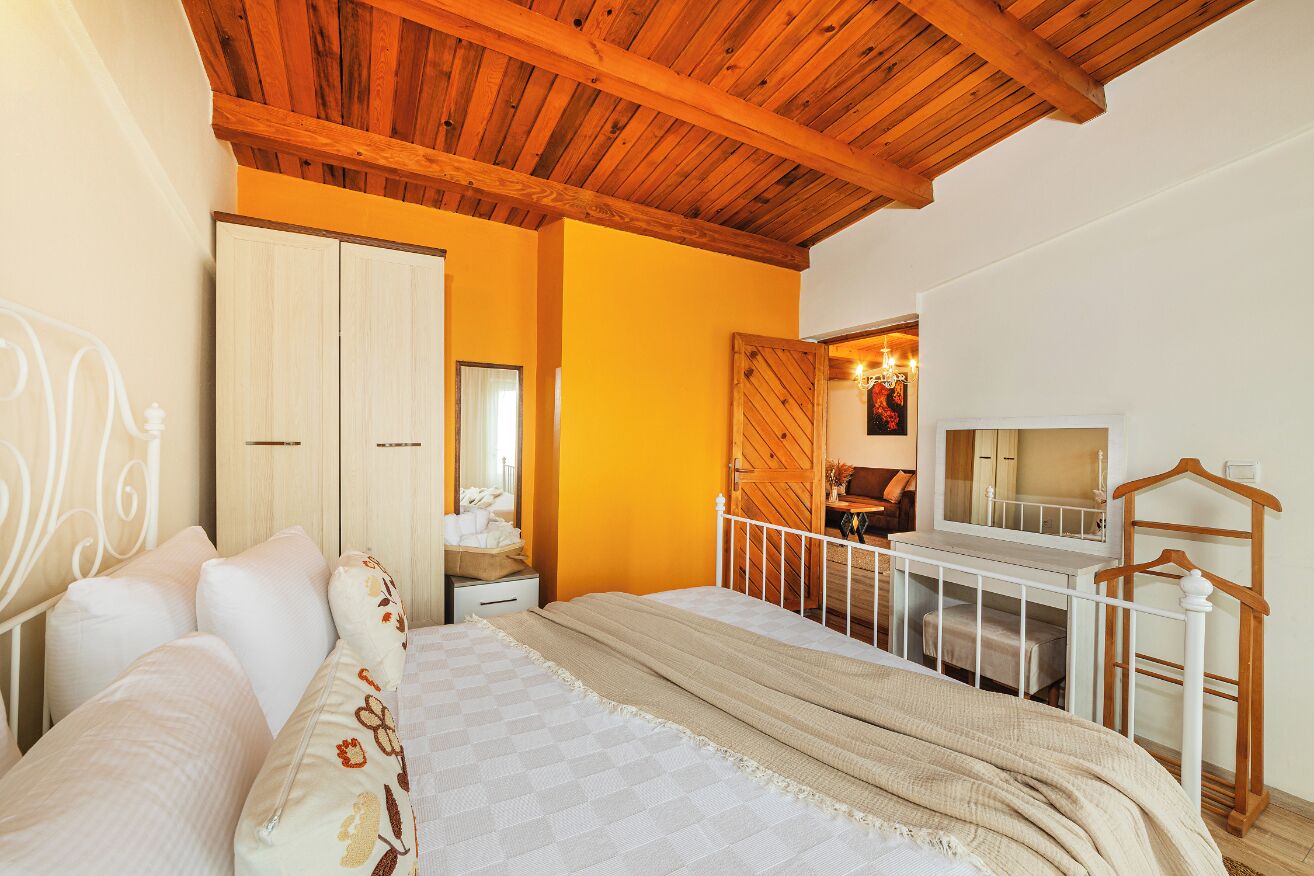 A bedroom with a wooden ceiling, a bed with white bedding, a wardrobe, and a desk with a chair.