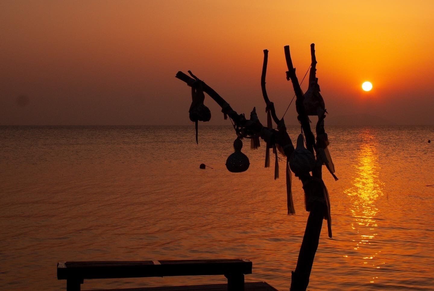 Un coucher de soleil sur l’océan, avec un banc au premier plan.