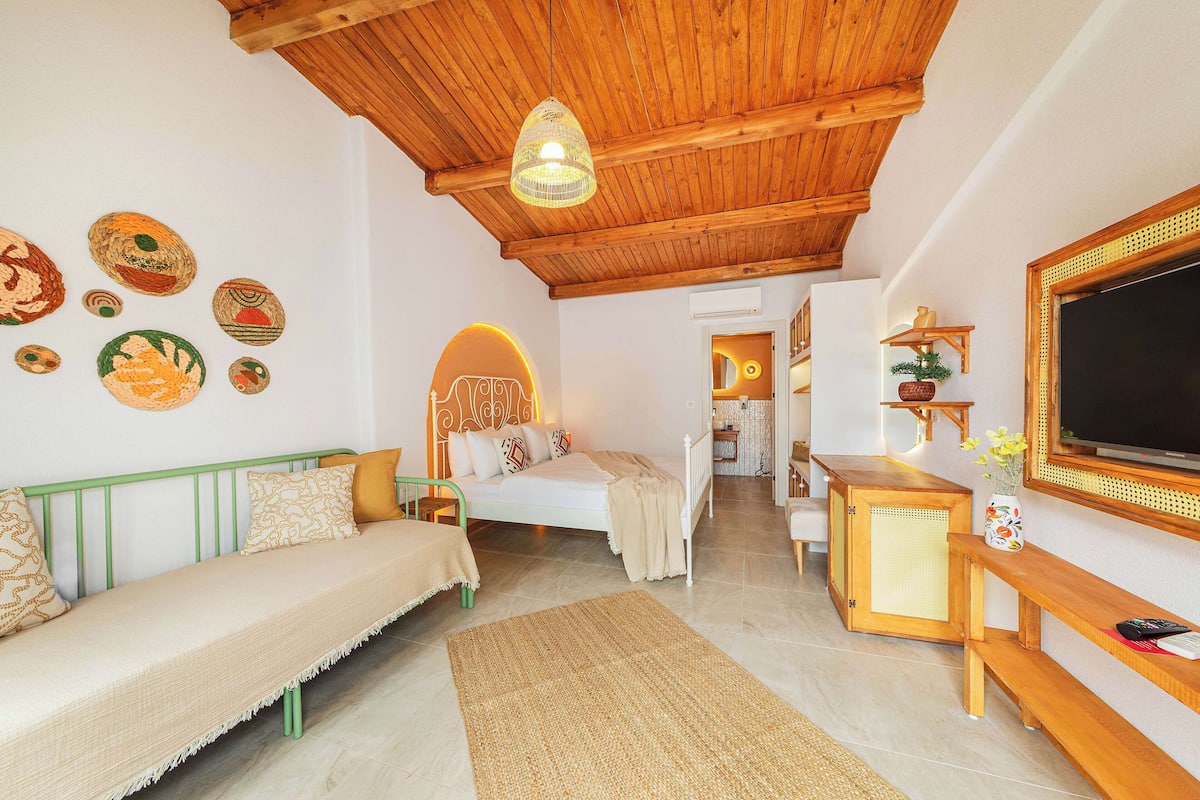 A cozy room with a bed, a green sofa, a wooden ceiling, and a TV on the wall.