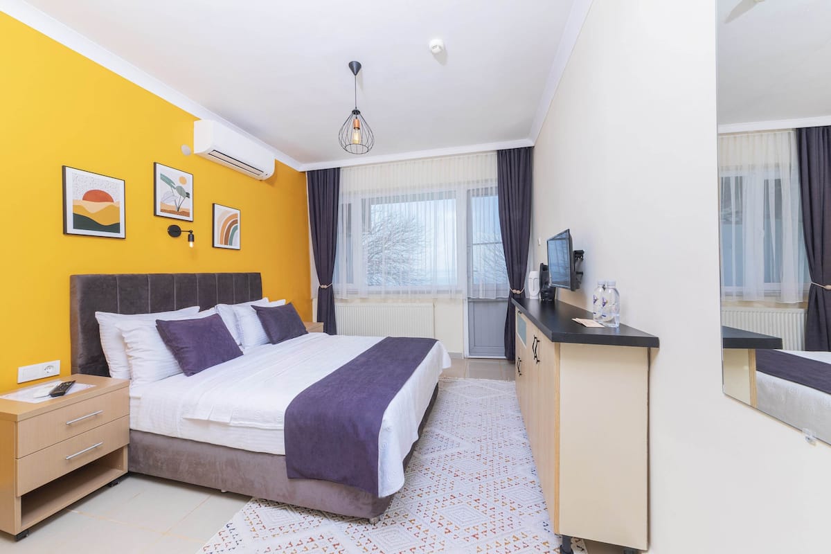 A hotel room with a bed, bedside table, dresser, and a large mirror.