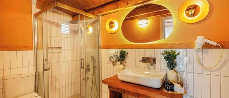 Een badkamer met een houten plafond, een douchecabine van glas, een witte wastafel en een spiegel met een ronde lamp.
