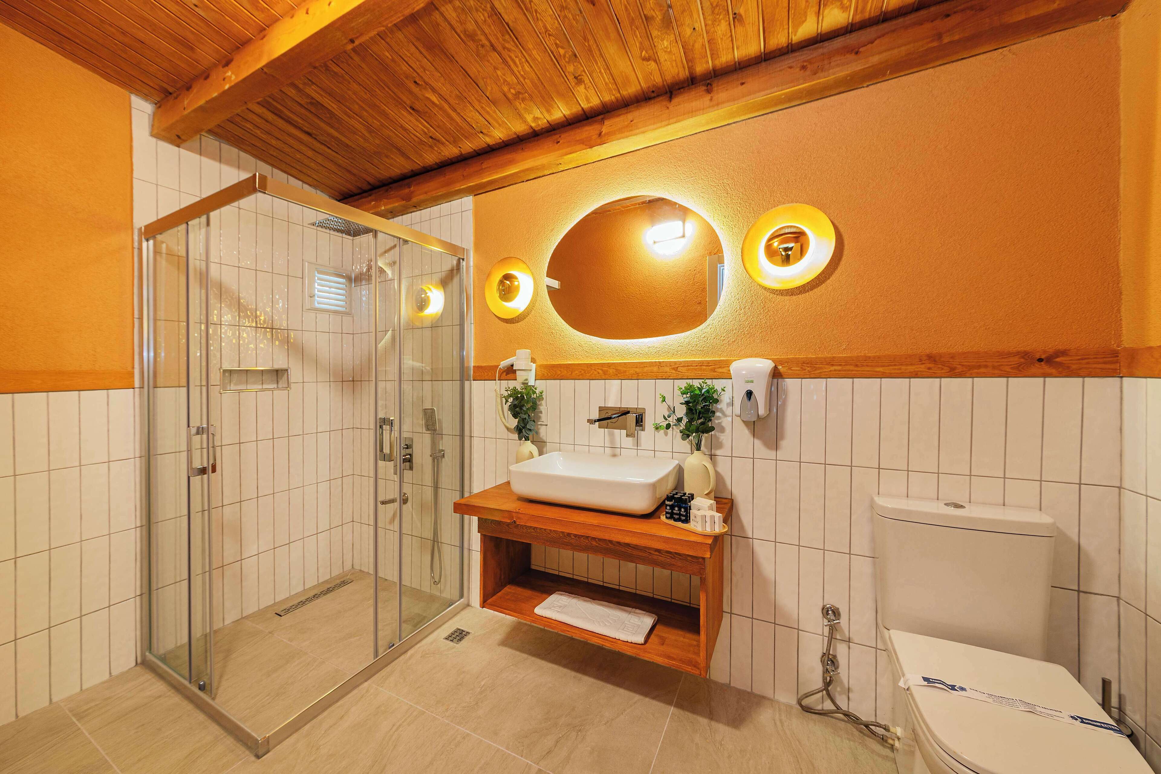Un baño con tocador de madera, cabina de ducha de vidrio y un inodoro blanco.