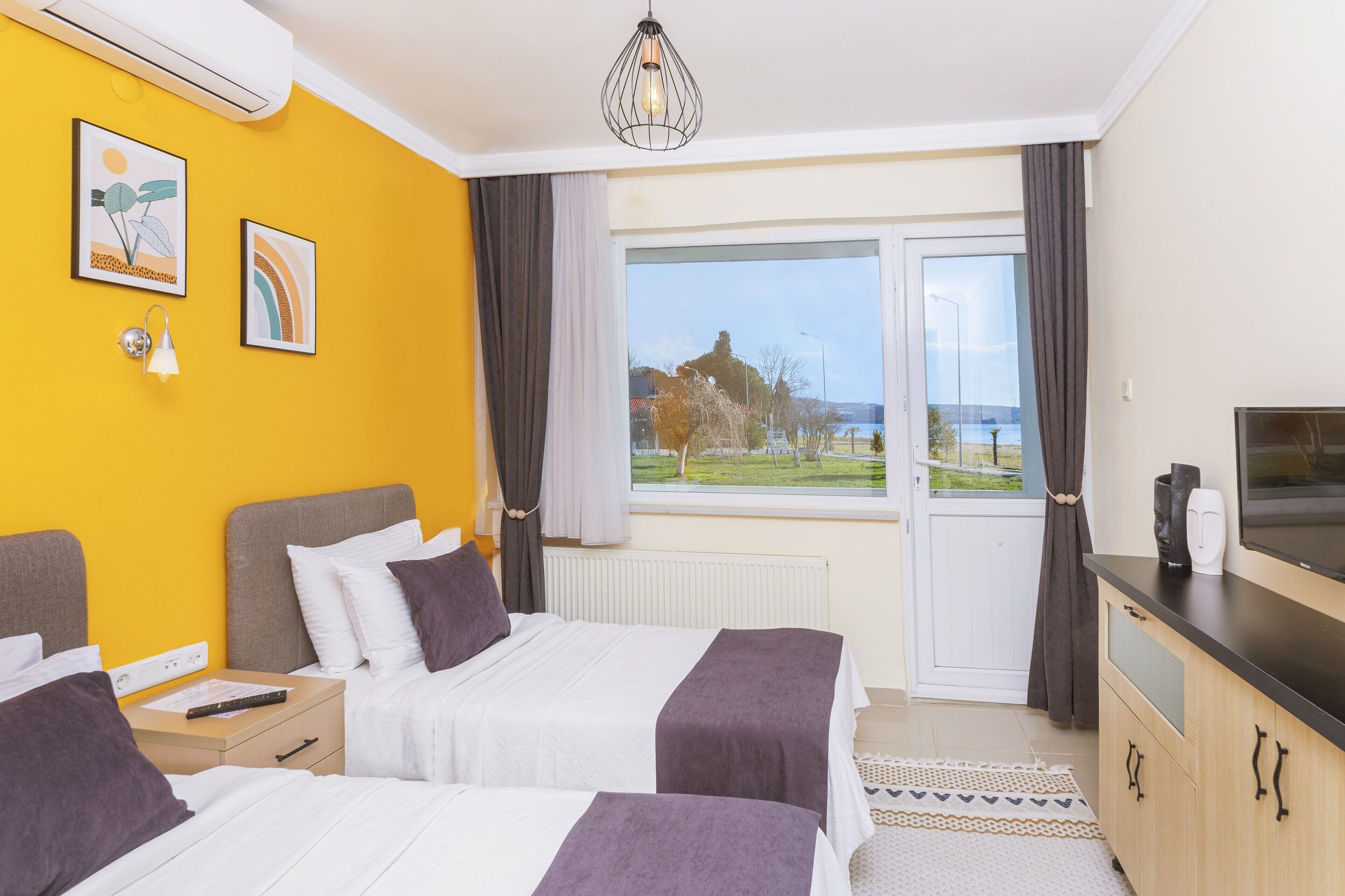 A hotel room with two beds, a large window with a view, a flat-screen TV, and a small cabinet.