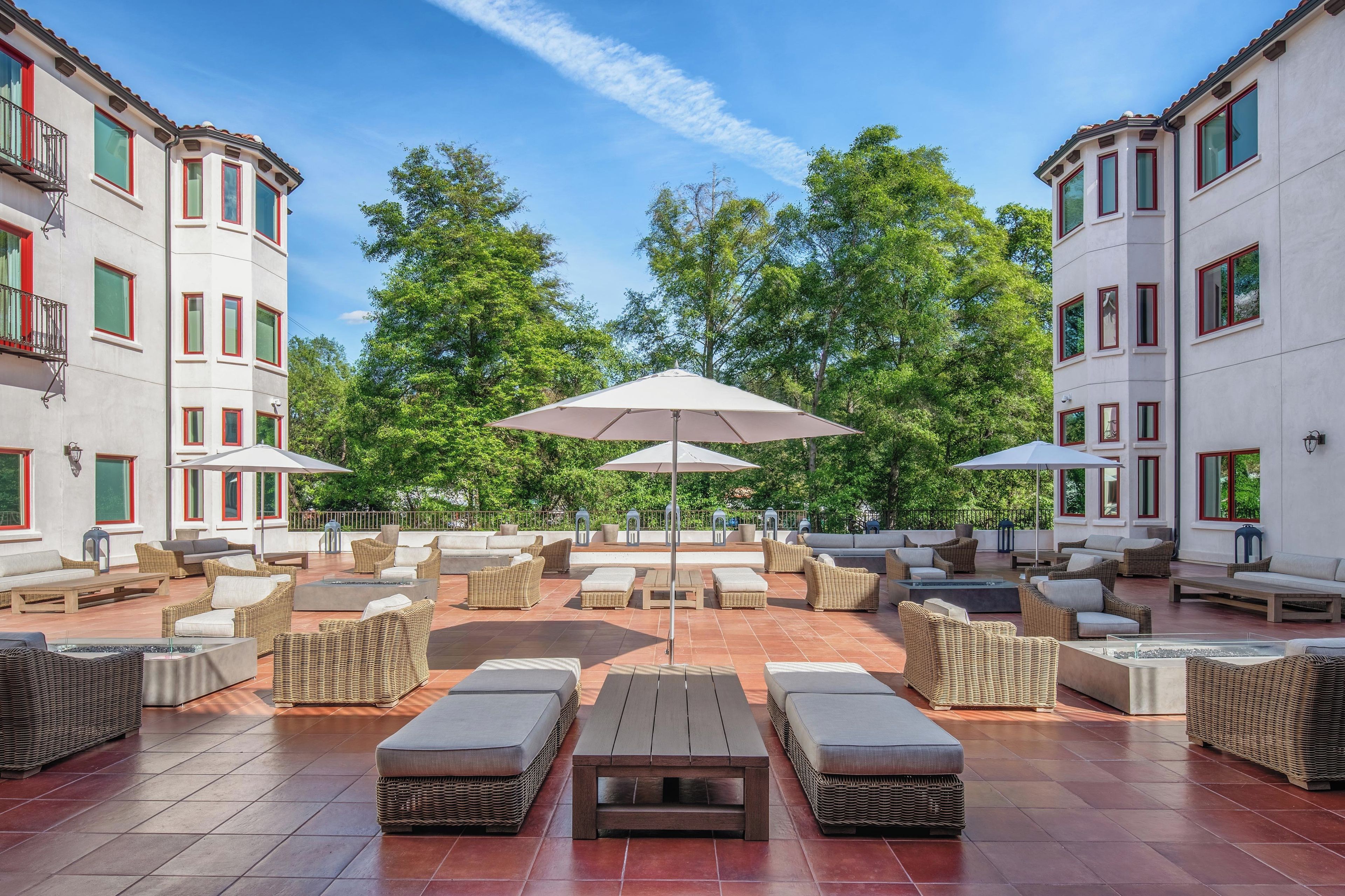 A spacious outdoor seating area with multiple tables and chairs, surrounded by trees and a clear sky.