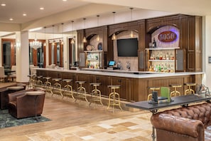 A bar area with a long counter, multiple stools, and a television screen. - Four Points by Sheraton Santa Cruz Scotts Valley (Scotts Valley)