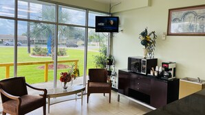 A hotel room with a large window, a television, a coffee machine, and a framed picture on the wall. - The Shades Motel (Baton Rouge)