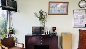 A hotel reception area with a desk, a clock, a framed welcome sign, and a window with a view of greenery. - The Shades Motel (Baton Rouge)