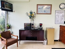 Zona de recepción de un hotel con mostrador, reloj, cartel de bienvenida enmarcado y ventana con vistas a la vegetación.