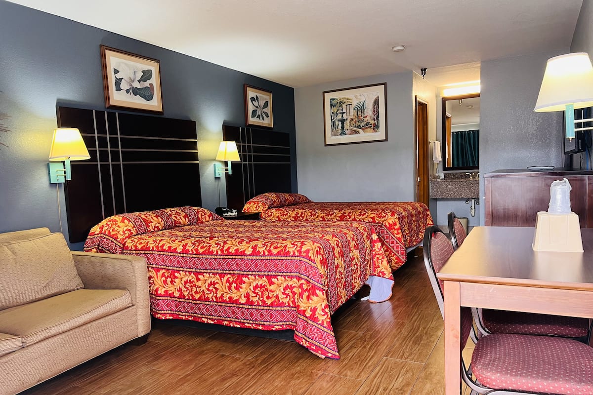 A hotel room with a bed, two bedside lamps, a chair, a table, and artwork on the walls.