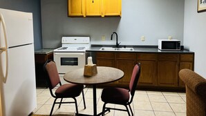 A compact kitchen with a refrigerator, stove, microwave, and wooden cabinets. - The Shades Motel (Baton Rouge)