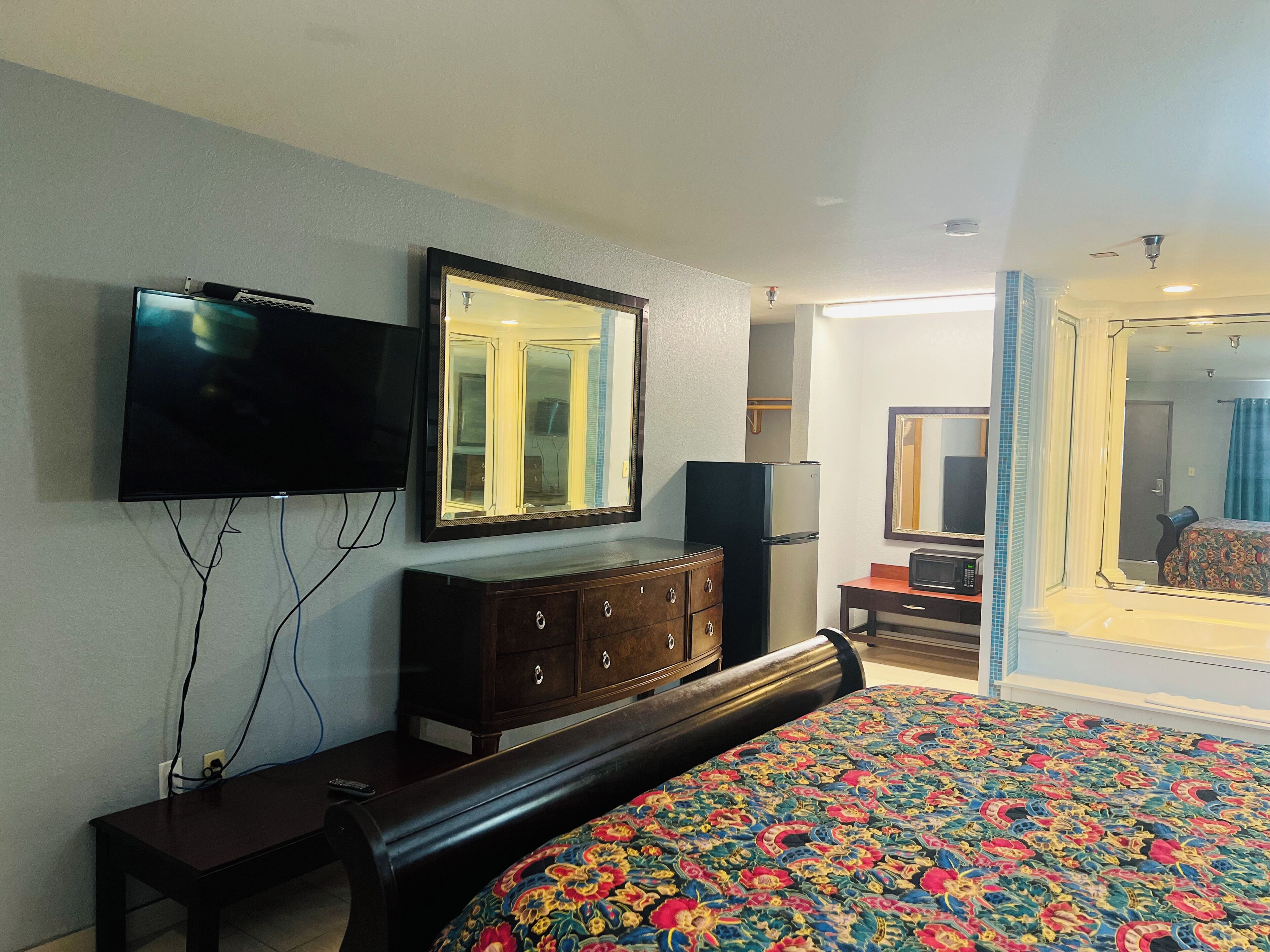 Une chambre d’hôtel avec un lit, une commode, une télévision et un miroir.