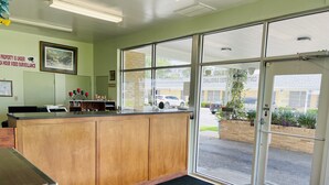 A reception area with a wooden counter, a framed picture on the wall, and a large glass door leading outside. - The Shades Motel (Baton Rouge)