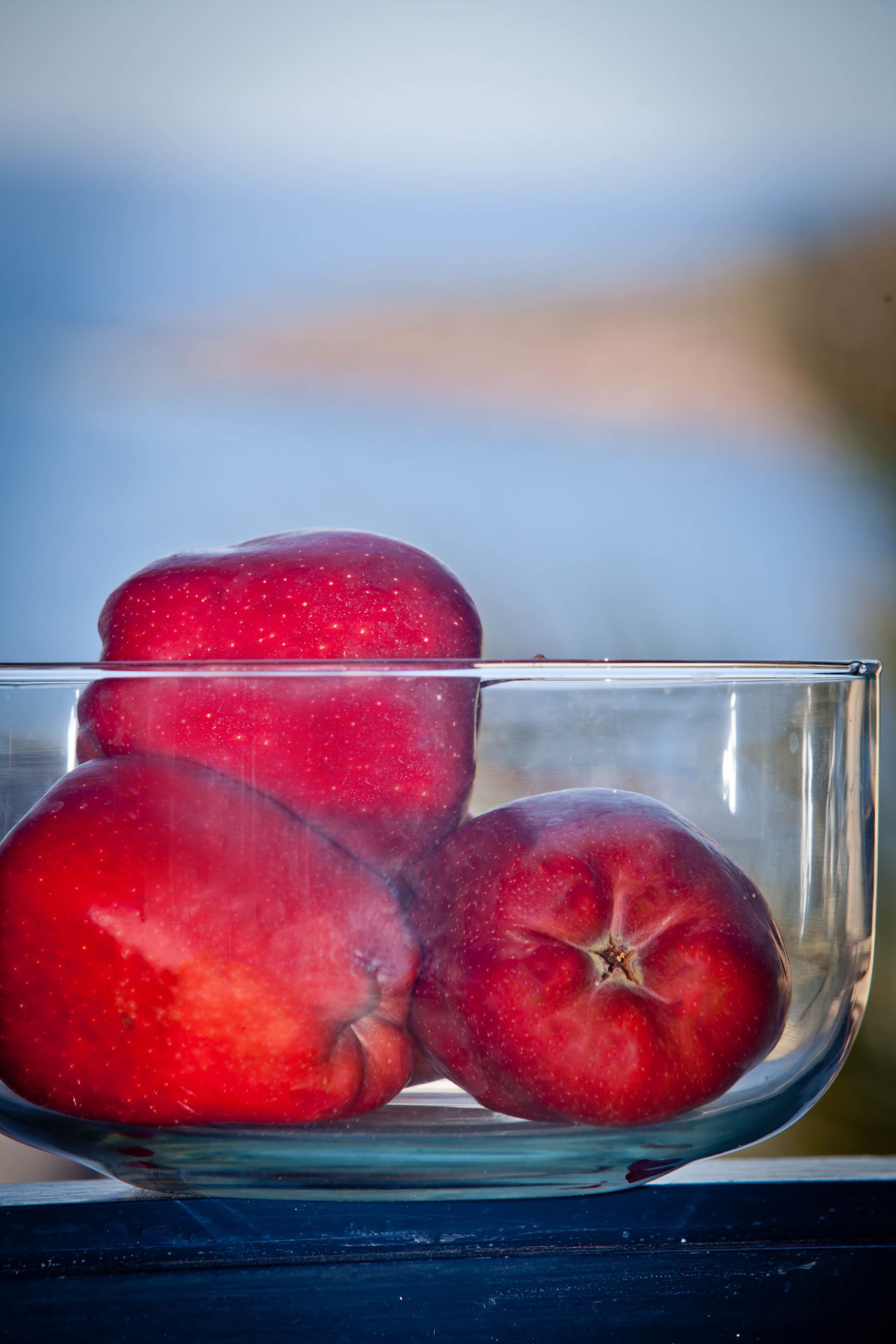 Un cuenco de vidrio transparente con tres manzanas rojas.