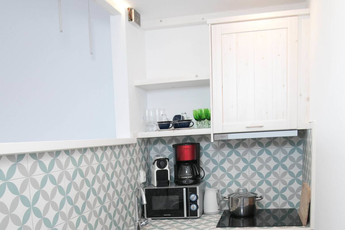 A compact kitchen with a patterned backsplash, a microwave, a coffee maker, and a small oven.