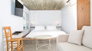Un dormitorio moderno con cama, una silla de madera, una mesita redonda y un sofá.