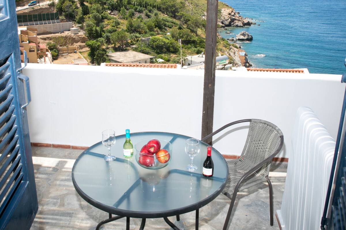 A balcony with a table and chairs overlooking a coastal view.
