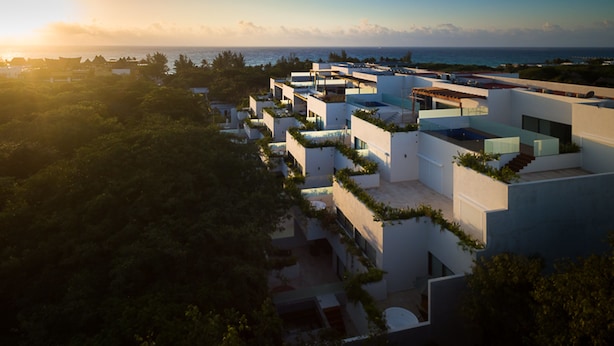 Een modern resort met meerdere witte gebouwen, zwembaden op dakterrassen en weelderige begroeiing.