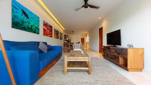 Een moderne woonkamer met een blauwe bank, een houten salontafel en een televisie op een houten dressoir.