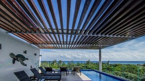 Een zwembadgedeelte met ligbedden, uitzicht op de oceaan en een pergola erboven.