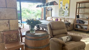A cozy living room with a wooden barrel, a beige armchair, a wooden bookshelf, and a painting on the wall.