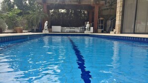 A swimming pool with clear blue water, surrounded by stone statues and a covered seating area.